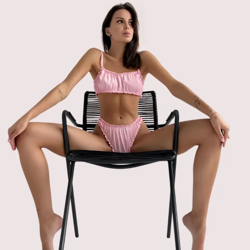 Pure silk bra and panty set in soft pink, seated pose showing adjustable straps and ruched fabric detailing.